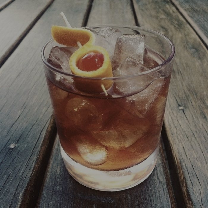An old fashioned on the bar, large cube, orange oil.